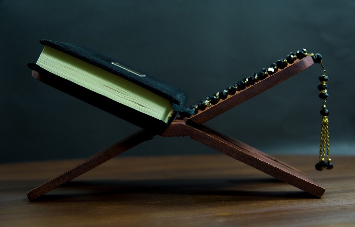 A Quran on a wooden reading stand beside prayer beads
